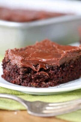 Zucchini Brownie on a white plate with fork in foreground and pan of them in the background