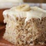 frosted banana cake with a banana on top on a wood plate