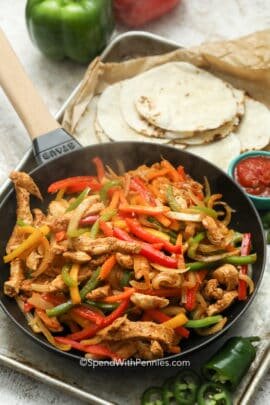 A pan of steaming chicken fajitas with tortillas on a pan with salsa and bell peppers