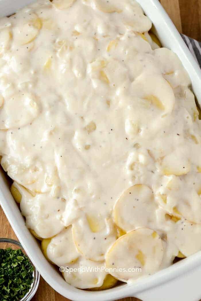 A pan of raw scalloped potatoes with parsley on the side