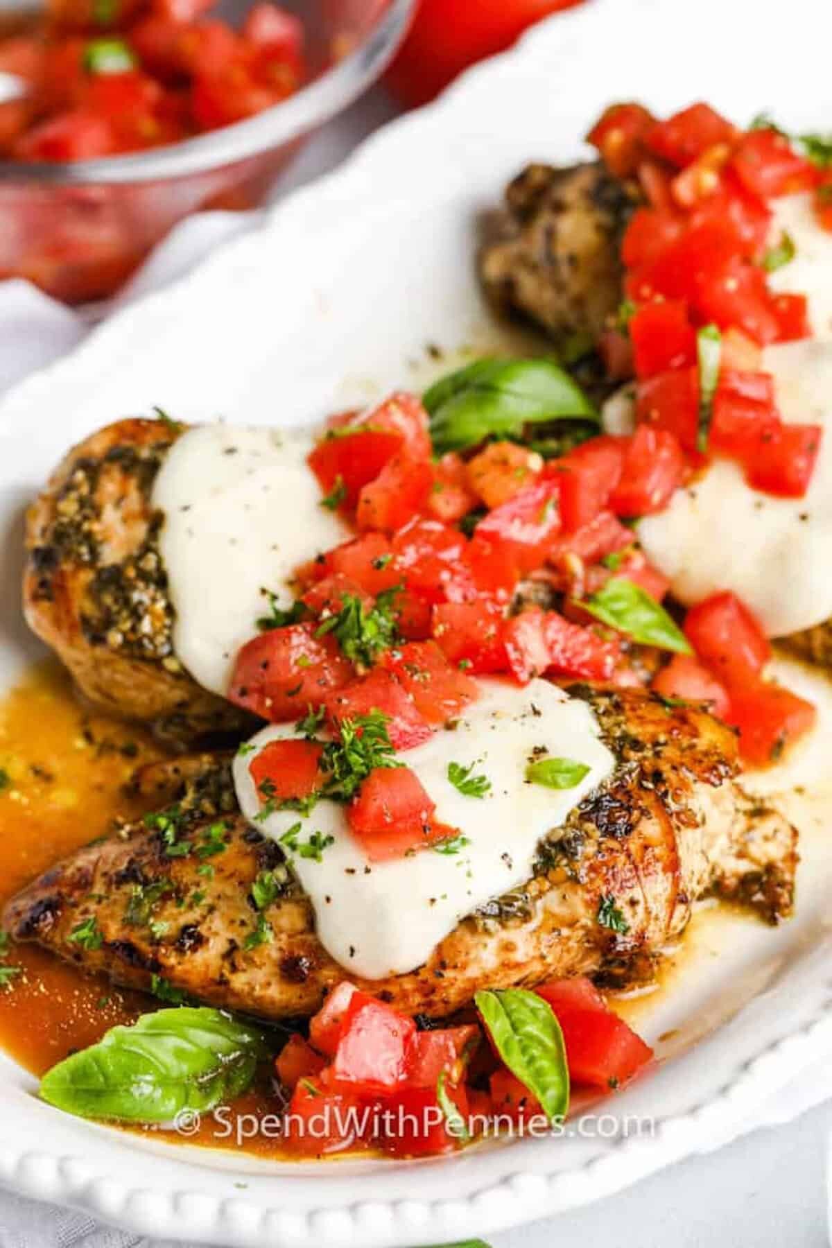 Pesto chicken on a plate topped with basil and tomatoes