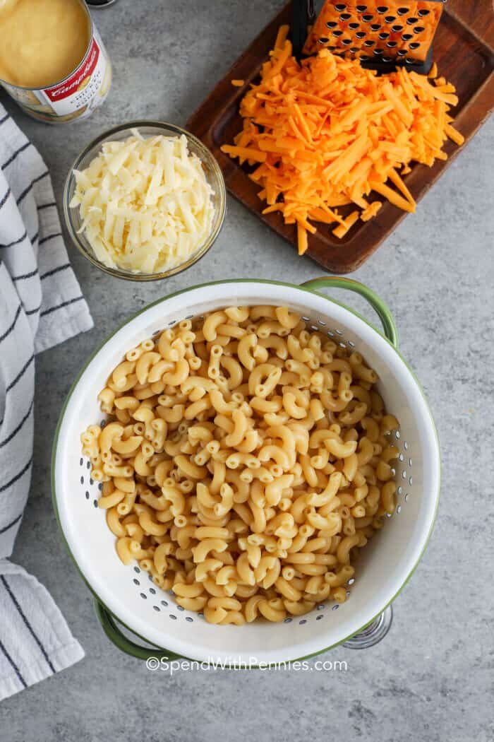 Pasta in a strainer with shredded cheese on the side