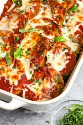 eggplant parmesan in a white dish with fresh basil as garnish